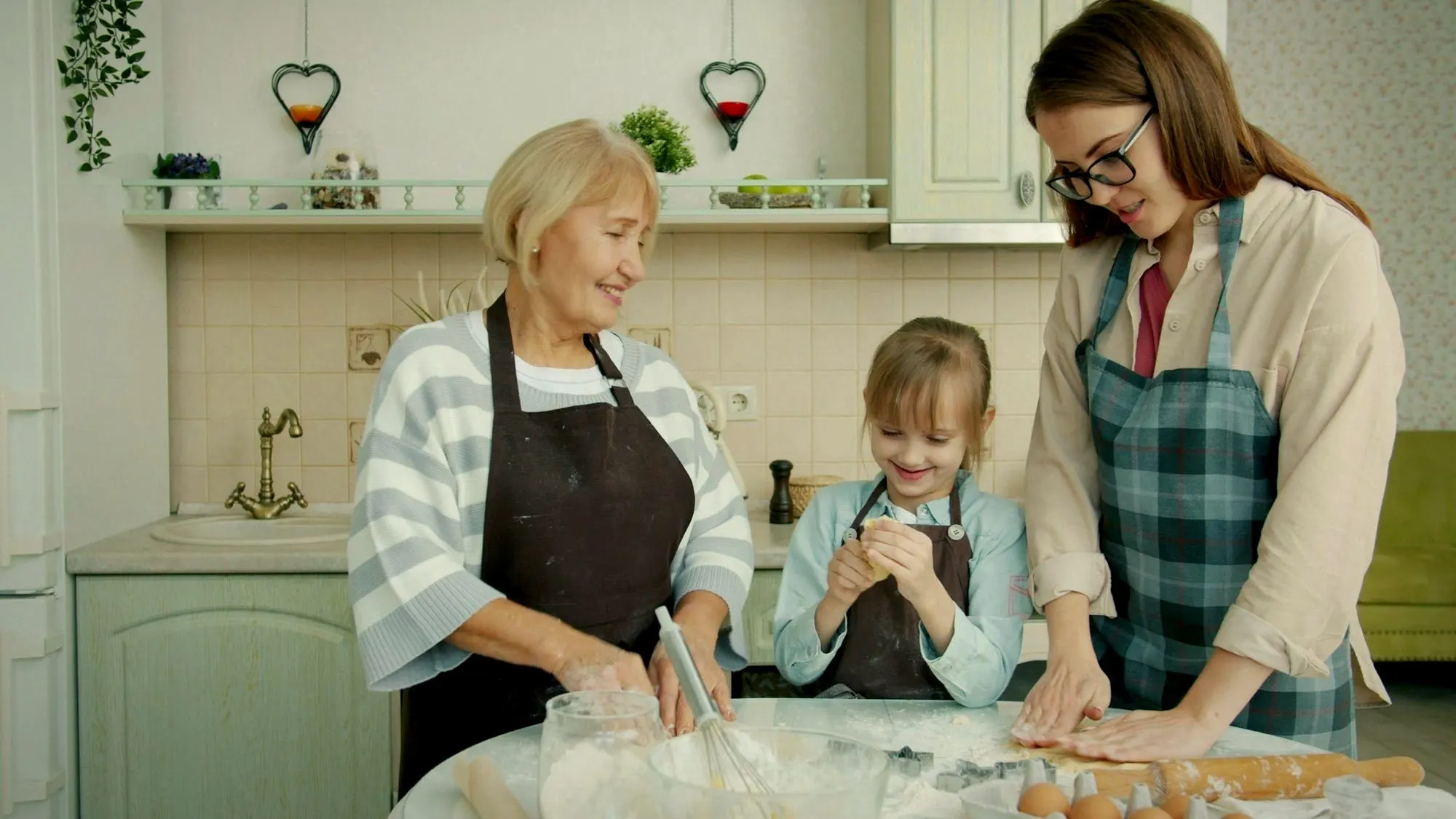 A grandmother, mother and daughter rolling out dough together in the kitchen