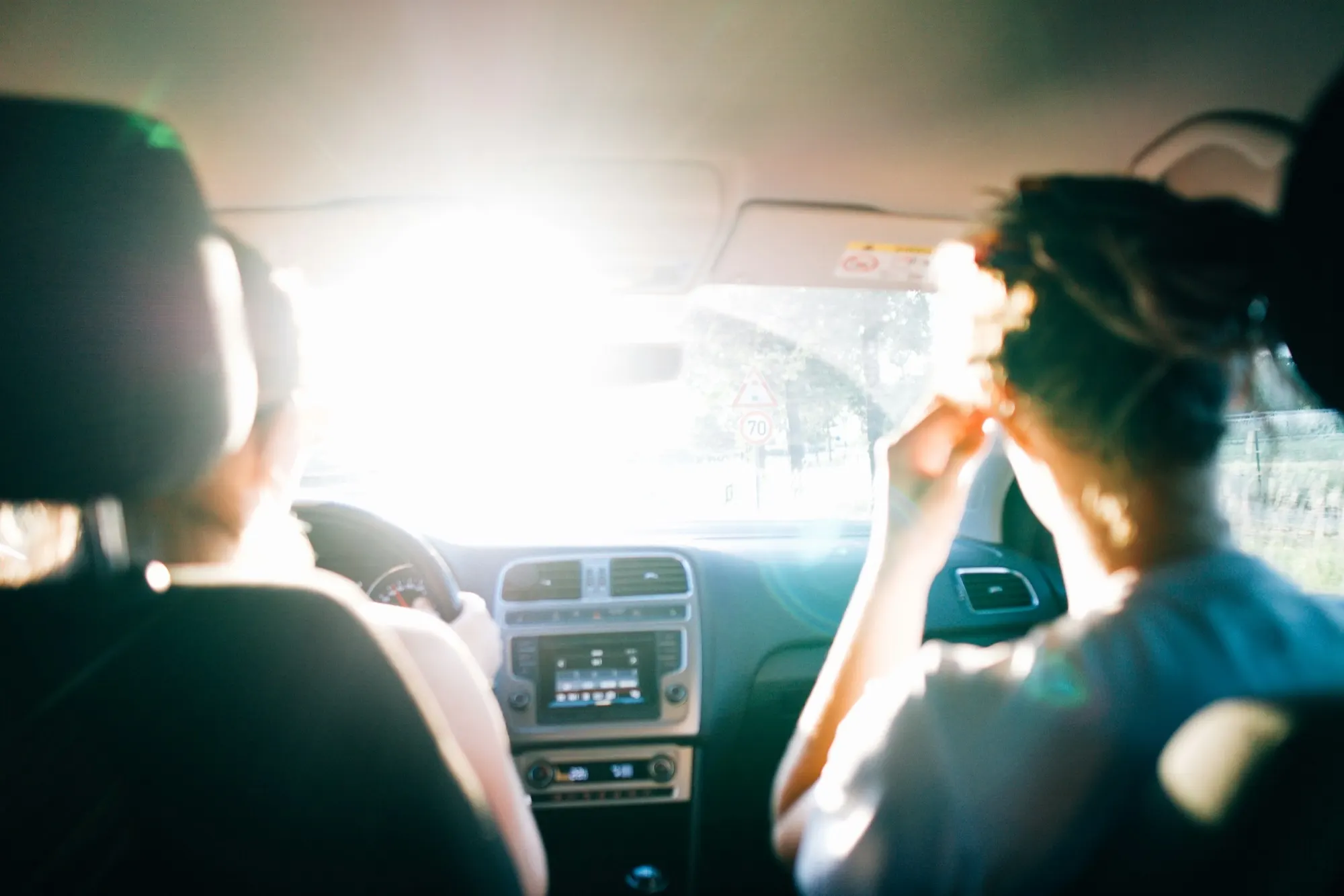 Two friends on a summer road trip, seen from the back seat as they drive into the sun